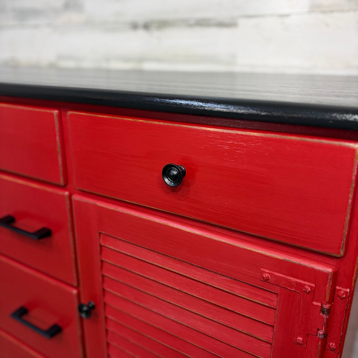 Closeup of black knob, distressed red finish, and louvered door hinges