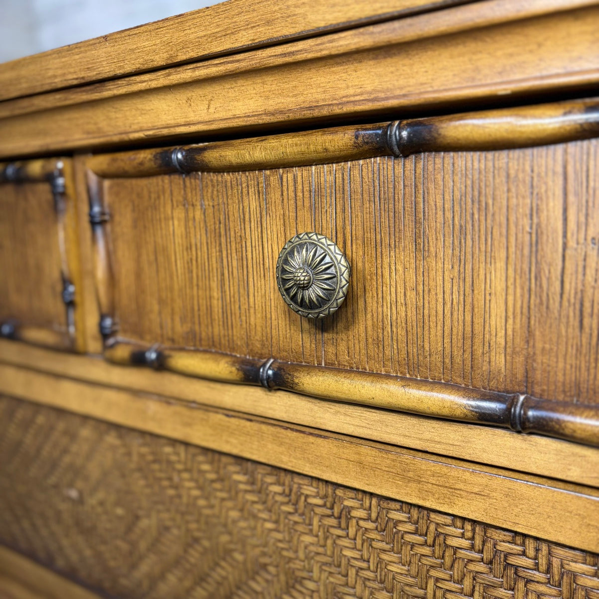 Closeup of pineapple-motif brass knob, bamboo trim, and woven rattan drawer front