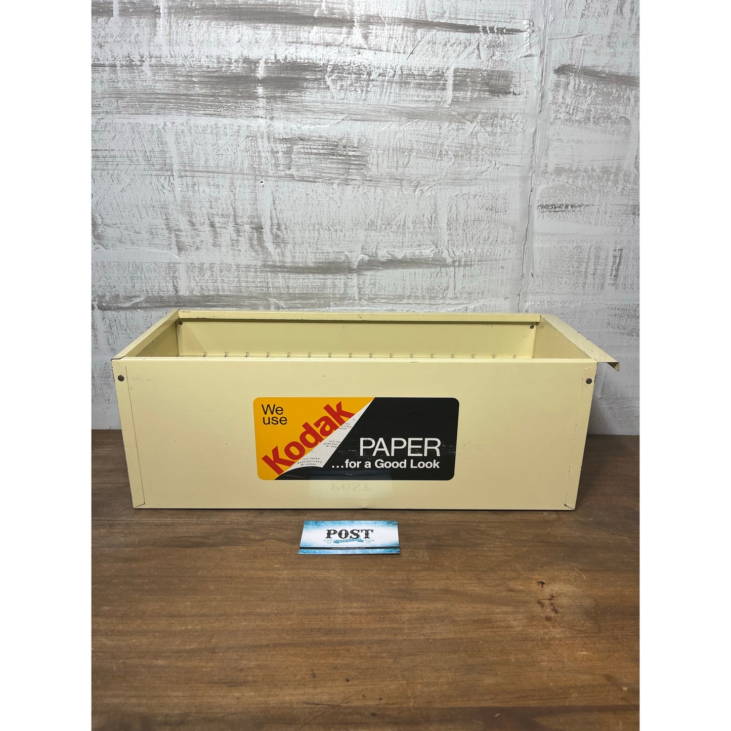 Vintage Kodak paper box on a wooden surface with a gray textured wall background