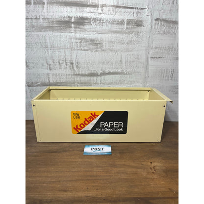 Vintage Kodak paper box on a wooden surface with a gray textured wall background